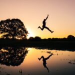 Action - silhouette photo of man jumping on body of water during golden hour