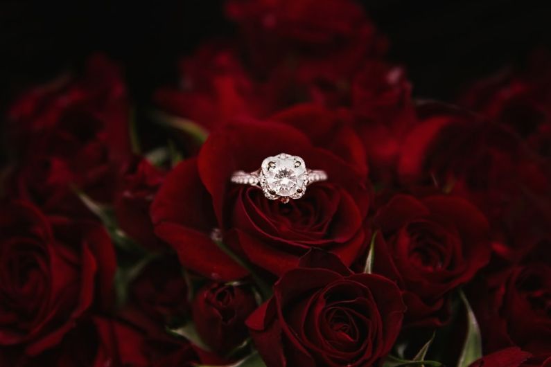 Engagement - silver-colored ring on top of red roses